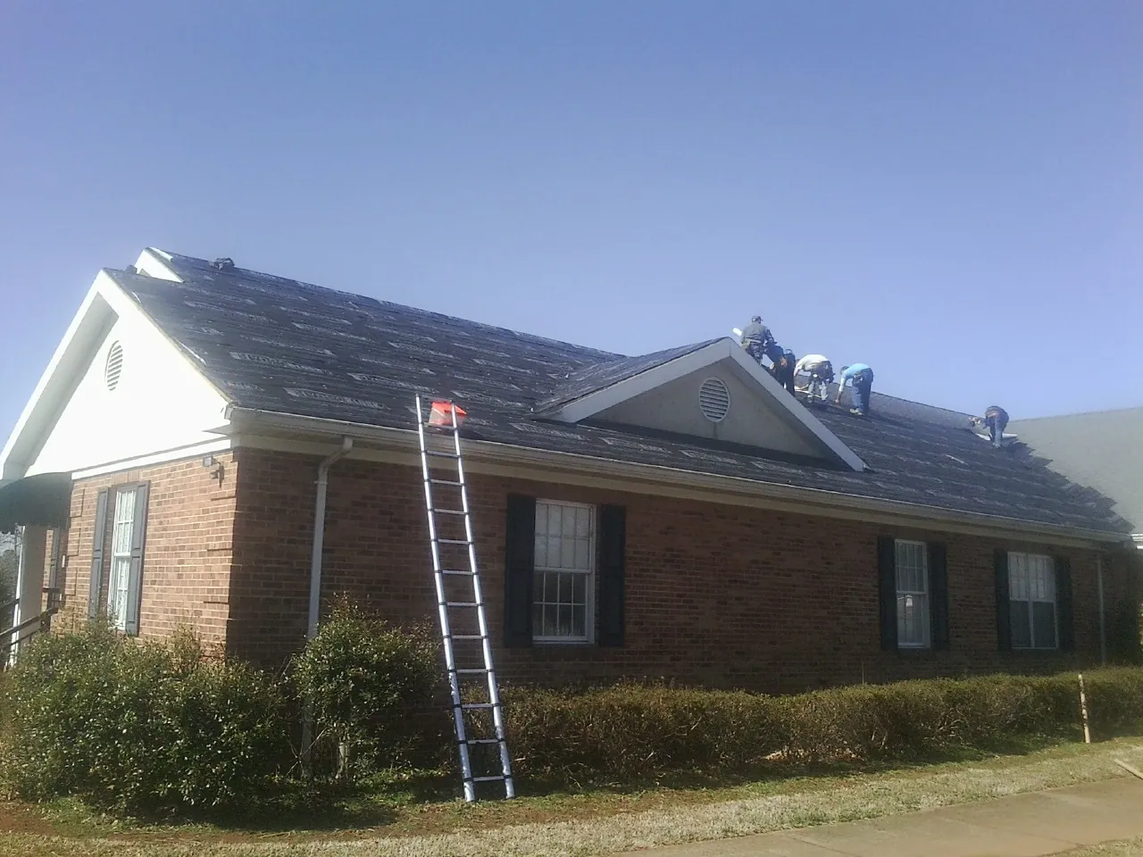 Crew tearing shingles off a brick ranch roof with a ladder set — Metal Roof Repair work by our crew in Spring Church