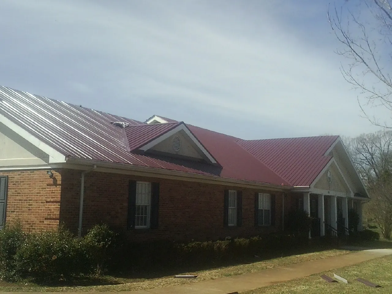 Red metal roof with gabled entries on a long brick building, from a Hail Damage Roof Repair job in Spring Church
