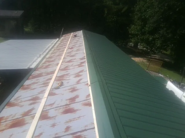 Old rusted panels beside newly installed green metal roofing — Wind Damage Roof Repair by Roofing Brothers in Spring Church