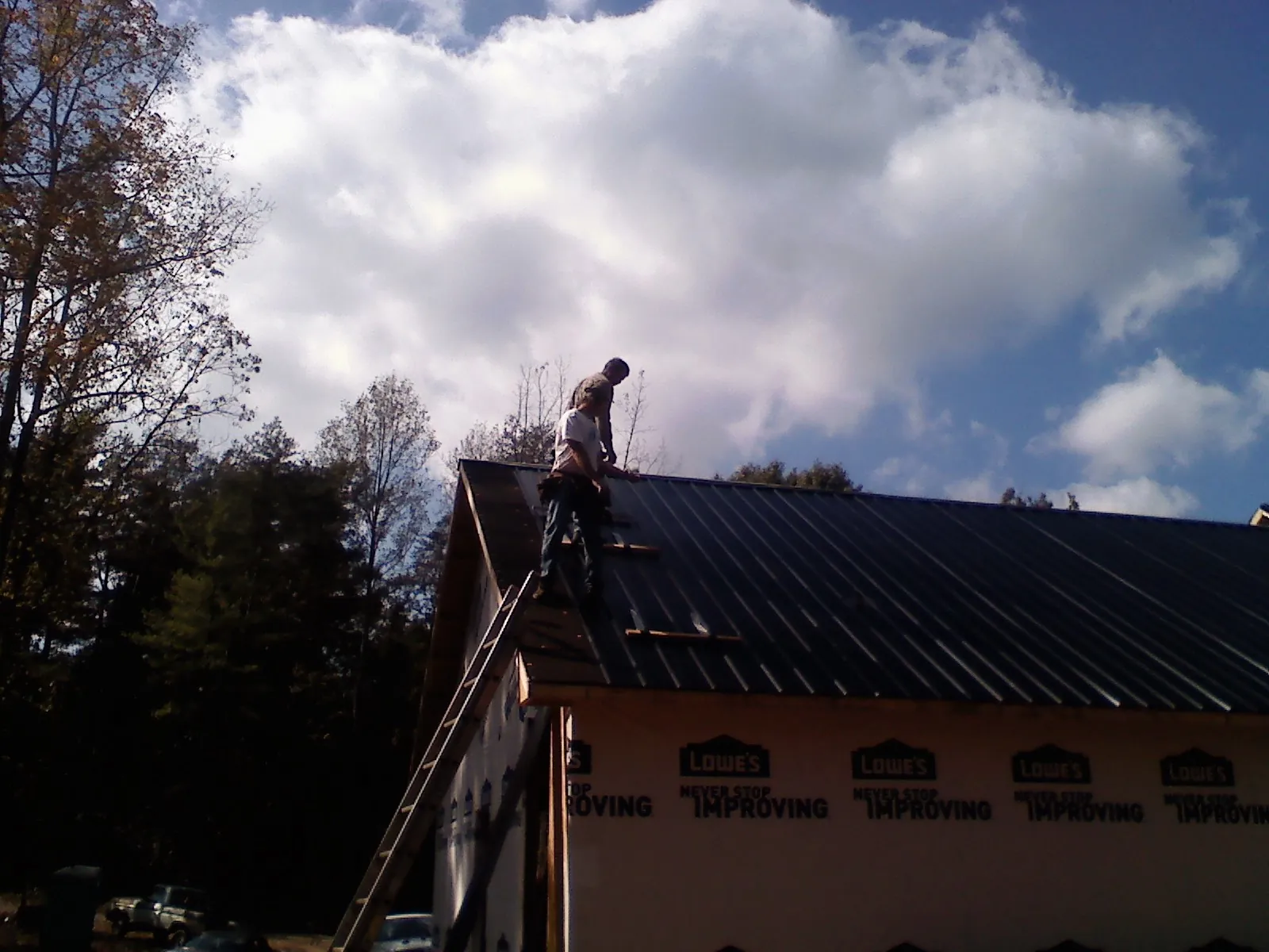 Roofer fastening dark metal panels high against a cloudy sky, from a Roof Inspection job in Spring Church