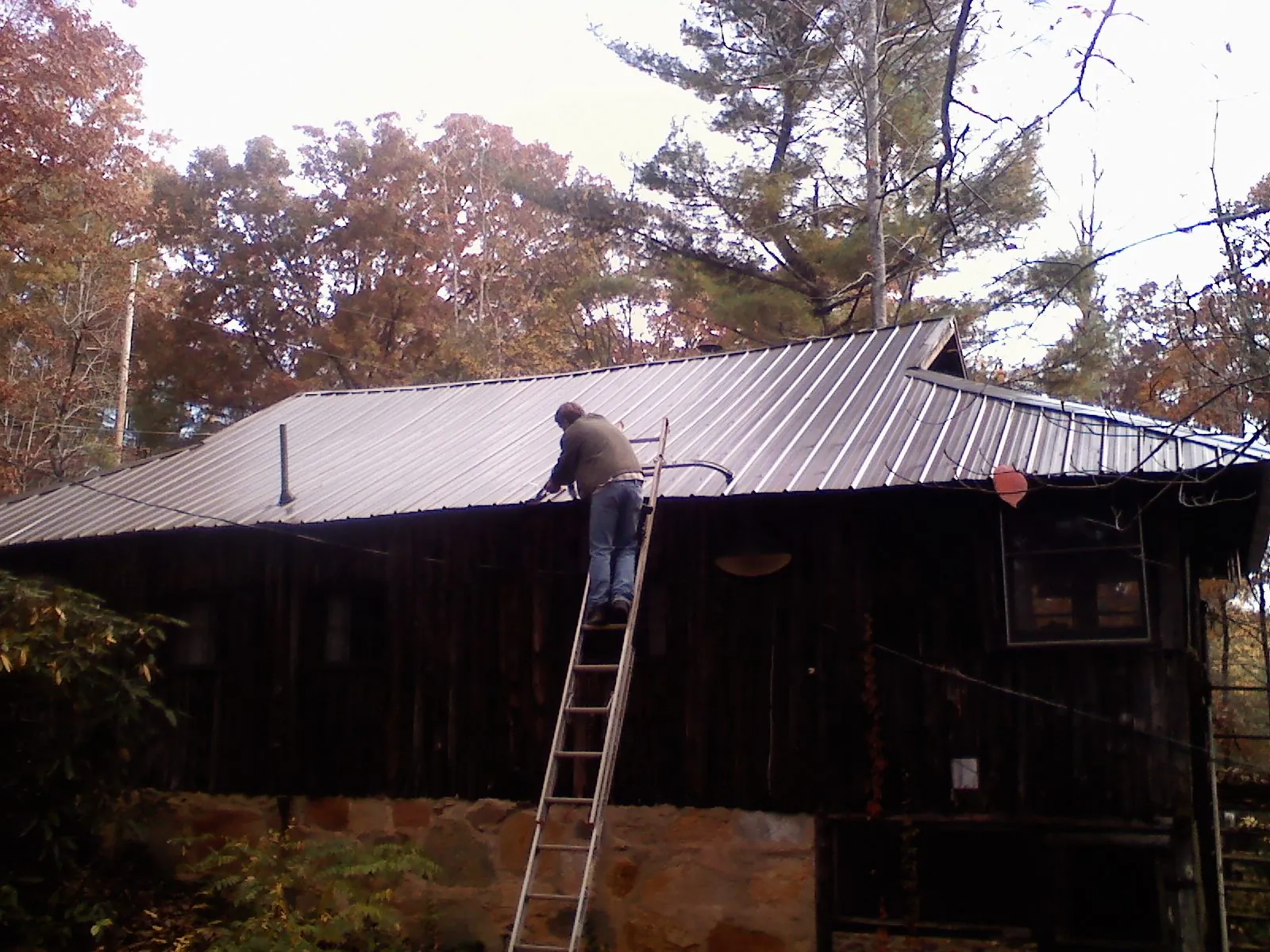 Roofer on a ladder working along the edge of a cabin metal roof in Spring Church