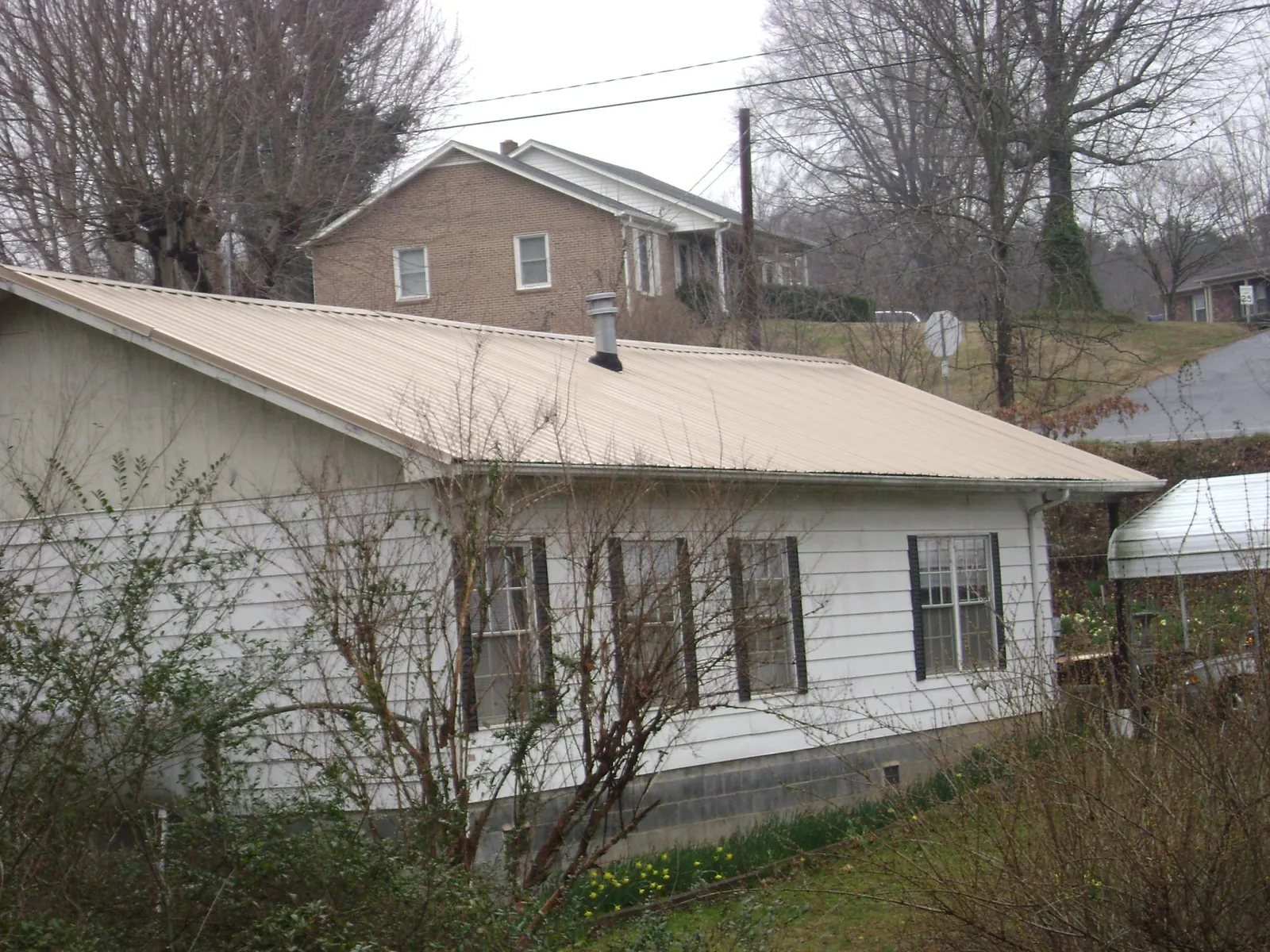 Tan metal roof on a white sided house set into a hillside — Commercial Roofing by Roofing Brothers in Spring Church