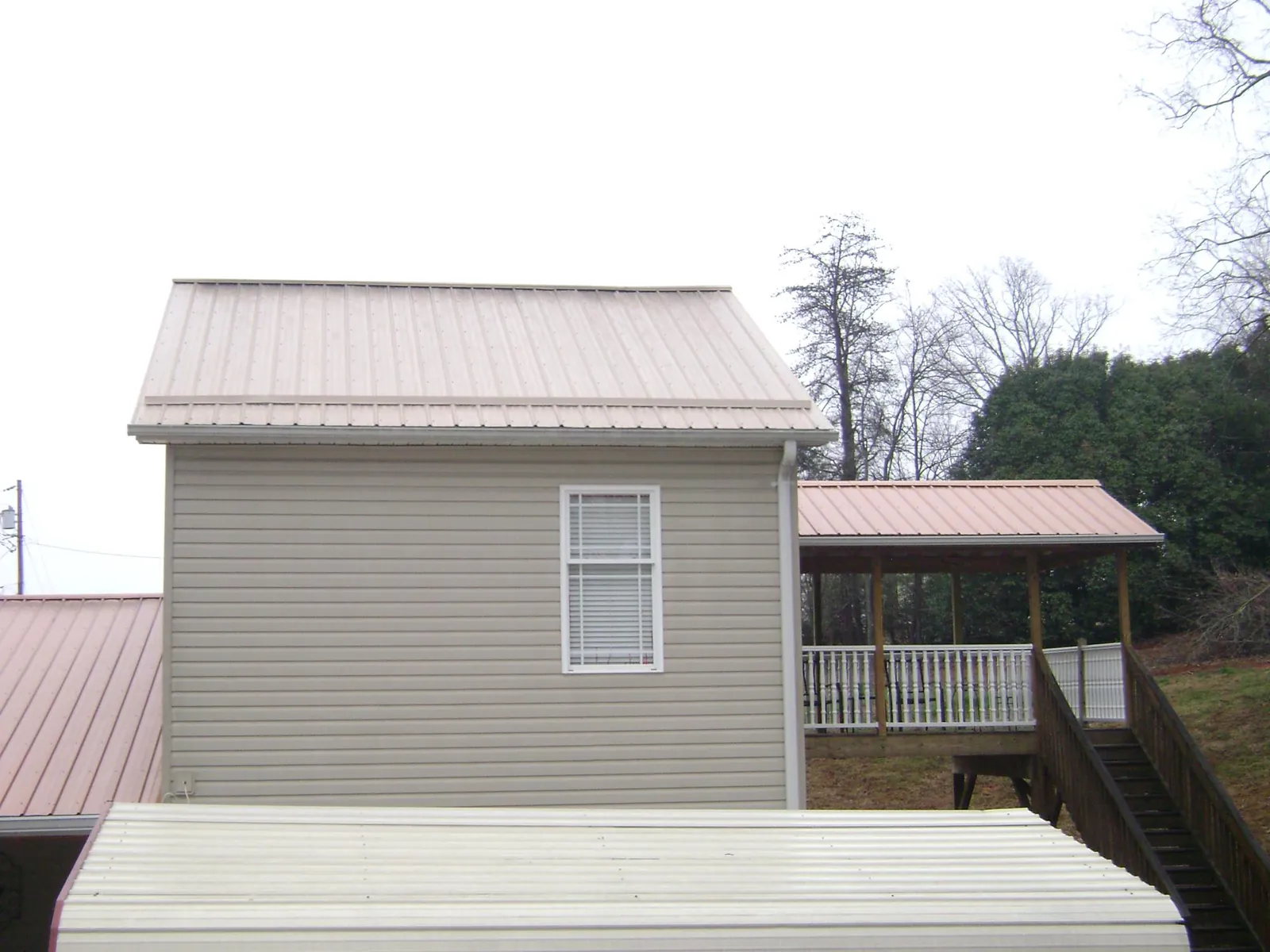 Tan metal roofs on a two story addition and attached porch, from a Roof Replacement job in Spring Church